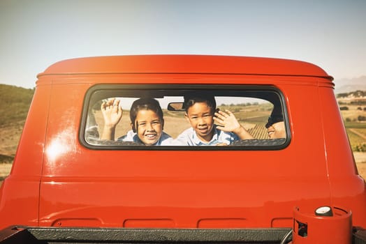 Smile and wave boys. two young cheerful boys smiling and waving from the back of a red pickup truck while looking into the camera.