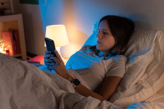 Beautiful young girl looking her phone on bed in the middle of the night. Technology at bed concept.