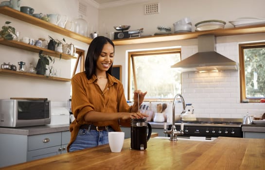 Young beautiful happy mixed race woman making herself some coffee in the morning. Content hispanic female in her 20s preparing coffee alone in the kitchen at home