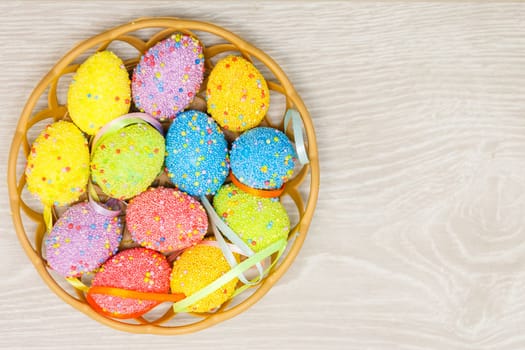 Colorful easter eggs in basket and mimosa flowers on wooden table. Top view with copy space