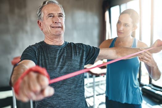 Exercise is vital for healthy aging. a senior man using resistance bands with the help of a physical therapist.