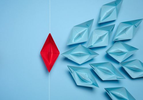 A group of blue paper boats and one red sailing against the current, concept of independent personality, breaking free from influence, strong leadership