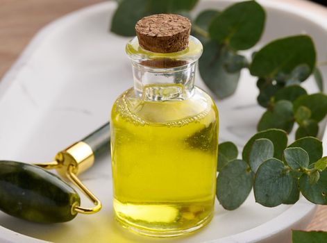 Transparent glass bottle with yellow oil and eucalyptus branch, cosmetic product