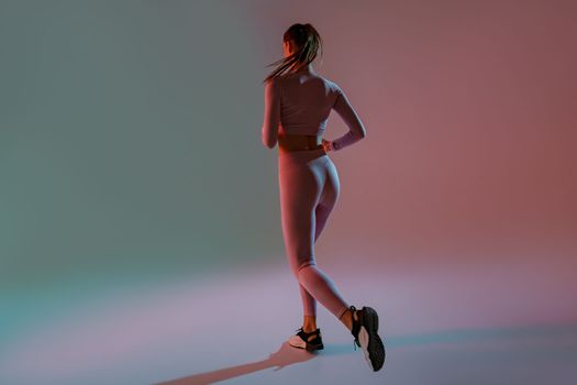 Back view of sporty woman running in Mid-Air exercising during cardio workout over studio background