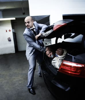 Get his head down. A gangster stuffing a bound and gagged businessman into the boot of his car.