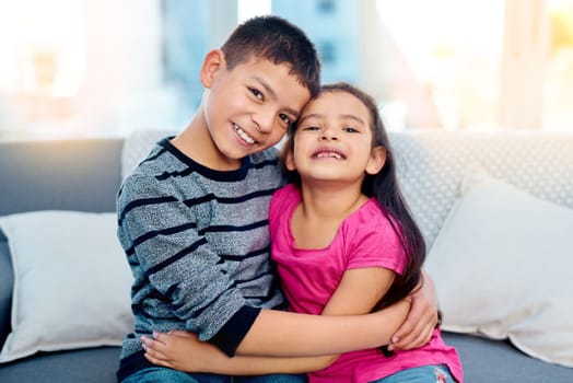 Nothing can tear them apart. Portrait of two adorable young children posing with their arms around each other while relaxing on a sofa at home.