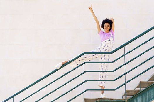 Optimistic black woman standing on staircase with raised leg