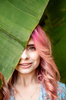 Woman portrait pink hair banana leaf. A beautiful young woman among the huge green leaves of a banana tree.