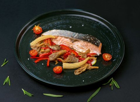 Fried salmon steak with vegetables on black table