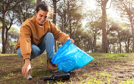 Happy young caucasian woman cleans forest picks up plastic bottle. Copy space.