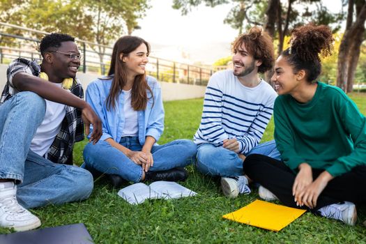 Multiracial college students study together sitting on campus grass. Friends talking in park.