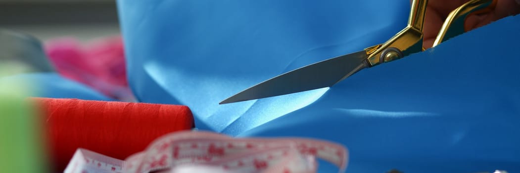 Woman hands cut blue fabric with tailor scissors closeup