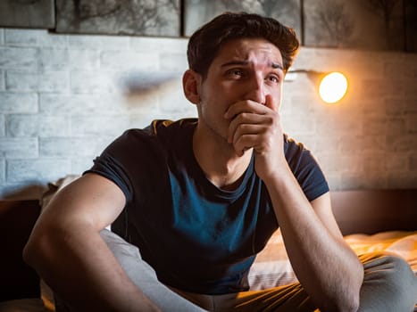 Man covering mouth while sitting on bed crying