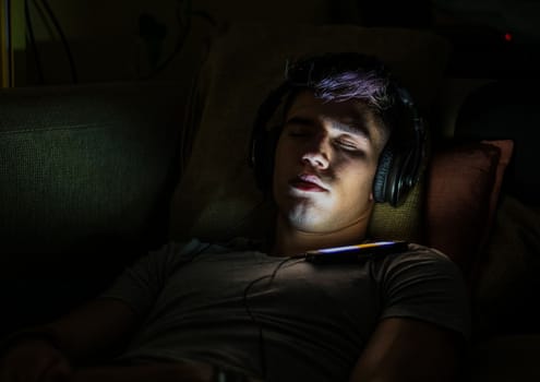 Man in headphones with smartphone sleeping at night
