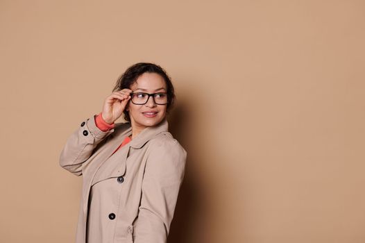 Sophisticated glamour lady in stylish black spectacles, looking aside over beige background with copy advertising space