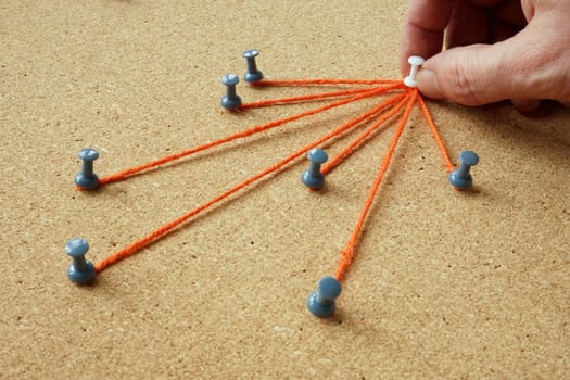 The pins are connected by a thread and the hand holds the main one. Delegating and leadership concept.
