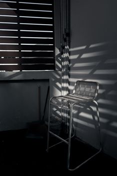 The white metal chair is affected by sunlight shine through the wooden blind. 