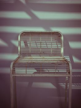 The metal chair is stand alone in front of the white wall with Sunbeam shine through in the morning. Retro style, 
