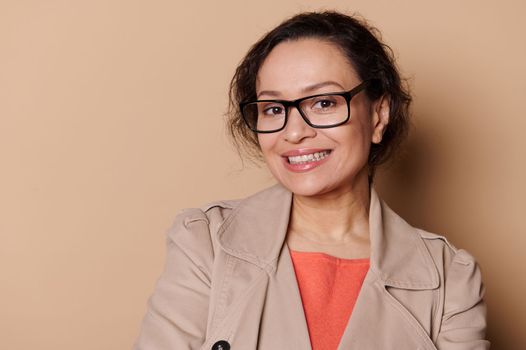 Closeup portrait of pretty woman wearing eyeglasses, smiling a toothy smile looking at camera, isolated cream background