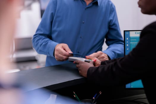 Elderly patient standing at registration counter paying with credit card for medication treatment and examination