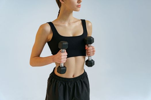 Close up of fitness woman doing exercises with dumbbells on studio background and looking at camera