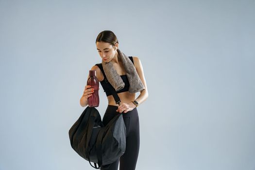 Sporty woman with sports bag and bottle of water after training on studio background
