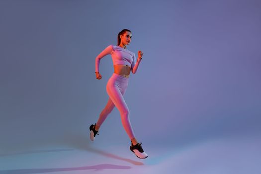 Pretty sporty woman running in Mid-Air exercising during cardio workout over studio background