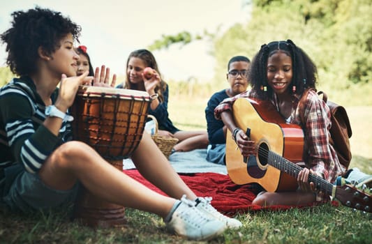 Gather round for a good jam sesh. a group of teenagers playing musical instruments in nature at summer camp.
