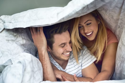 Delightfully in love. a happy young couple having fun under a duvet in bed.