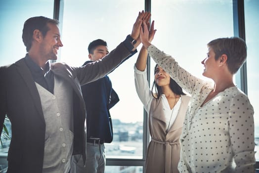 Feeling the spirit of their collaboration. a diverse group of businesspeople high fiving in an office.