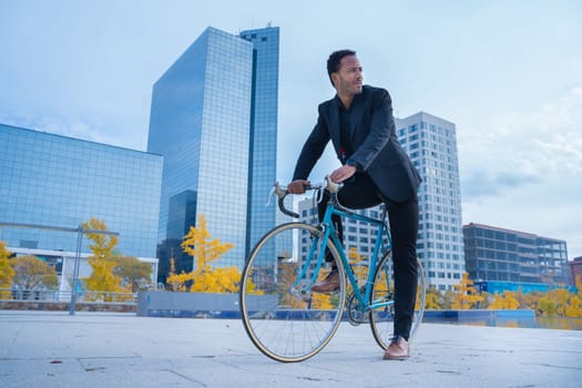 Stylish African American businessman in suit going to the office by bicycle in financial district. Business and transport concept. High quality vertical photo
