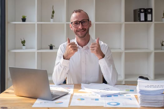 Business man at the office success sign doing positive gesture with hand, thumbs up smiling and happy. cheerful expression and winner gesture