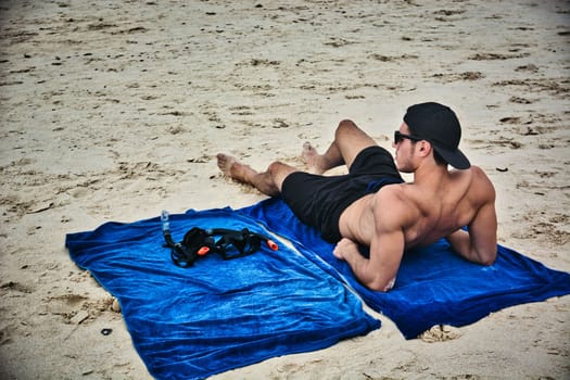 Half body shot of a handsome young man laying on a tropical beach in Thailand