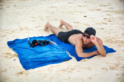 Half body shot of a handsome young man laying on a tropical beach in Thailand