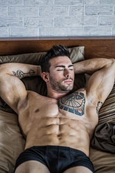 Shirtless muscular sexy male model on bed, relaxing with eyes closed