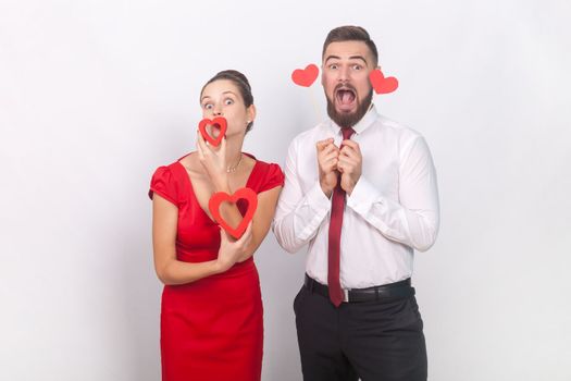 Funny screaming man and woman in red dress with pout lips standing together, holding hear figures.