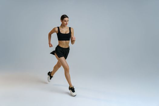 Sporty determined woman running during cardio workout over studio background