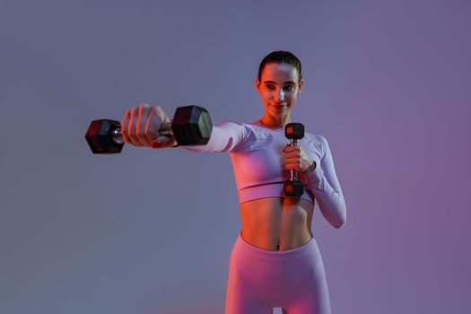 Pretty fitness woman doing exercises with dumbbells on studio background. Strength and motivation