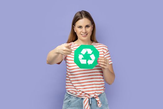 Woman holding green recycling sign and pointing finger to camera with toothy smile.