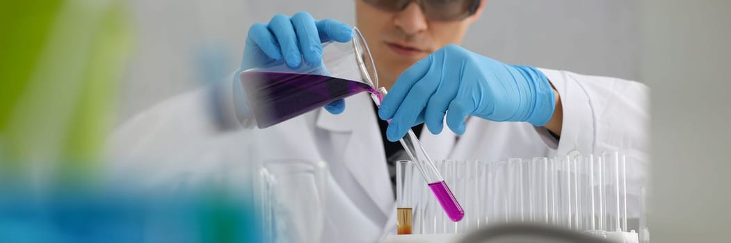 Scientist in protective gloves holding test tube of purple liquid