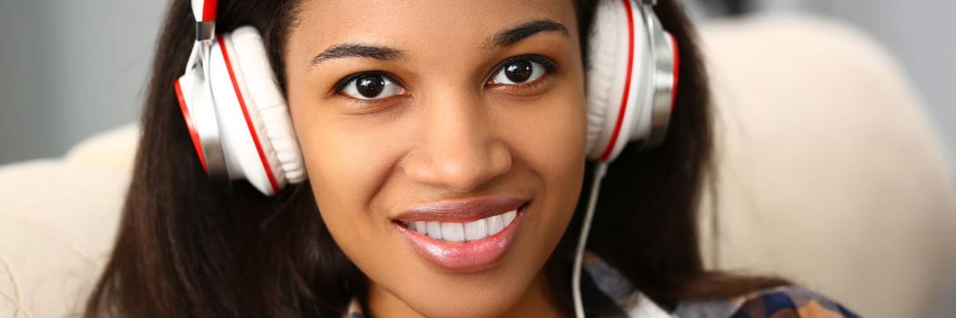 Smiling woman with headphones on sofa and listening to music