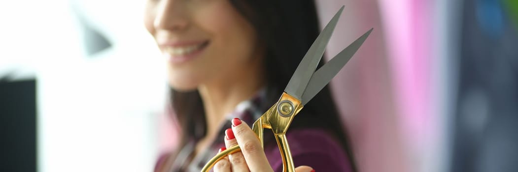 Young woman smiles and stands in tailor workshop with scissors in hand