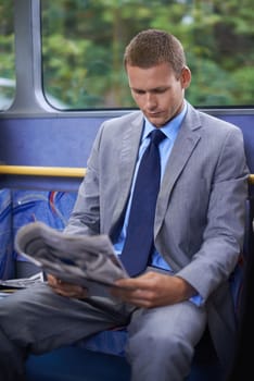 Time to play catch up. a young businessman reading a newspaper on a bus