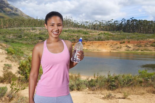 Stopping for a drink. A young ethnic jogger standing outside holding a water bottle.
