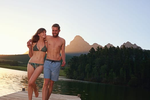 Love and laughter at the lake. an affectionate young couple in swimsuits walking on a dock at sunset.