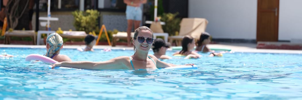 Young woman in sunglasses swims with aqua noodles in pool