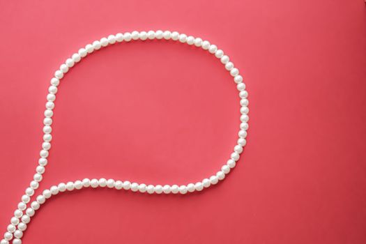 Chat message bubble made of pearl jewellery necklace on coral background