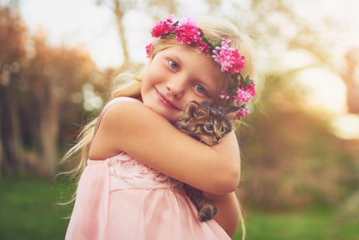 Warm hugs for my feline friend. a happy little girl holding a kitten and looking at the camera outside in the nature.