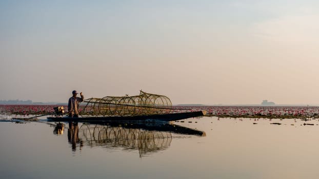 Fishermen in a boat at Sunrise at The sea of red lotus, Lake Nong Harn, Udon Thani, Thailand February 2023