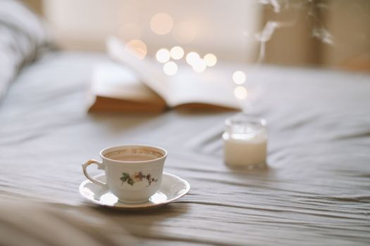 Light cozy bedroom, Coffee or tea cup and an open book on the bed. Spring still life. Breakfast in bed.